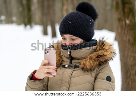 Girl taking photos with mobile phone during winter vacation trip in snowy winter forest