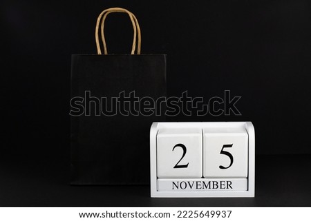Paper bag and November 25 on a wooden calendar, black background. Black Friday The concept of sale, promotion, shopping, shops, gifts, text, holiday, poster, layout,business,copy space, market,
