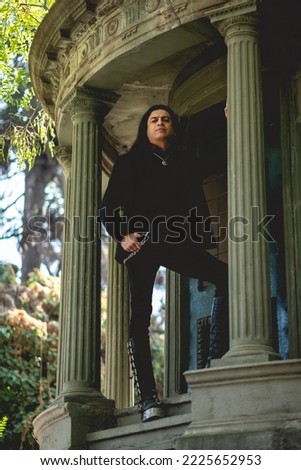 Dark gothic man with long hair in large ancient abandoned mausoleum in neoclassical style with columns and stairs in the forest