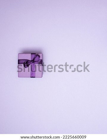 Purple gift box with ribbon on pastel purple background with copy space. Creative realistic minimal gift for Christmas or Holiday giving. Present with bow as Christmas gift.