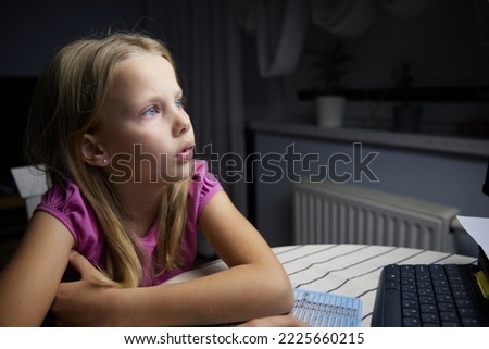 A smiling little European girl looks at the monitor screen and smiles.