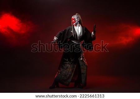 A young woman in fantastic makeup and an Asian kimono, the image of a cyber geisha. Full - length photo , dancing on a dark background with red backlight