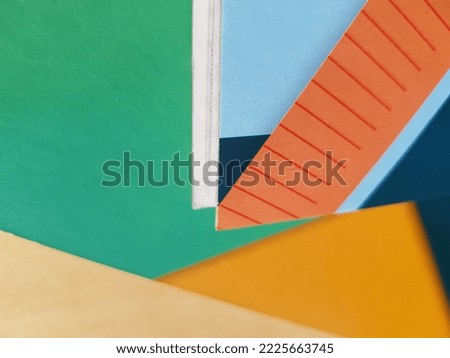 Multicolored covers of notebooks with a geometric print, in the sun, chaotically superimposed on each other (macro, top view, texture).