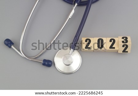 Changes in medicine and health care in year 2023. Stethoscope and numbers 2022 and 2023 on wooden cubes on gray background. 