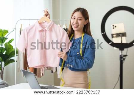 vlogger, blogger small SME business asian beautiful woman using mobile phone video call for sell clothes live stream selling online, show product present detail at home office, entrepreneur ecommerce Royalty-Free Stock Photo #2225709157
