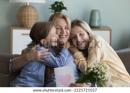 Grandma embrace little granddaughter, thank adult daughter for gift on birthday, holding spring chamomile flowers and postcard, smiling feel happy. Live events, Mothers Day and 8-march celebrations Royalty-Free Stock Photo #2225721037