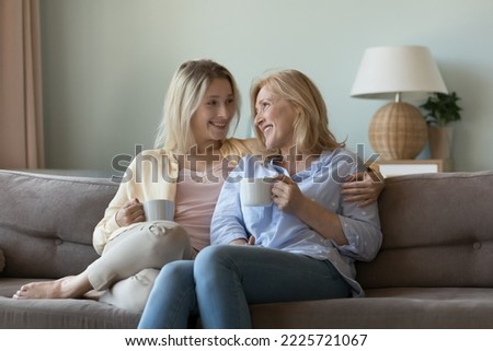 Understanding, harmonic relationships between older mother and grown up millennial daughter. Two different generation female sit on couch with teacups smile enjoy pleasant talk and warm communication Royalty-Free Stock Photo #2225721067