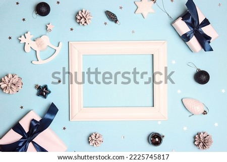 Blank white photo frame surrounded by festive decorations on a blue background. Christmas, New Years top view concept with copy space.