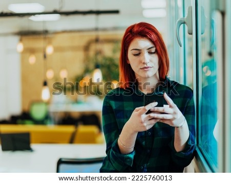 Headshot portrait of modern woman in office at night near window using smartphone