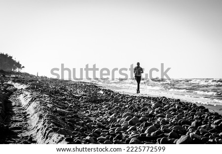 Black and white photography of Baltic seascape of Latvia with sea pebbles in forefront and blurred running woman in the distance