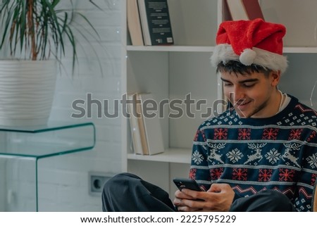 young man at home with christmas clothes looking at mobile phone