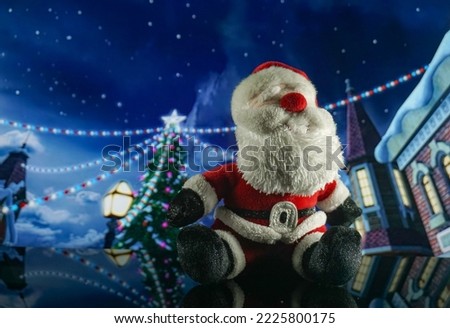 Santa claus doll with snowy village background and christmas decorations at night