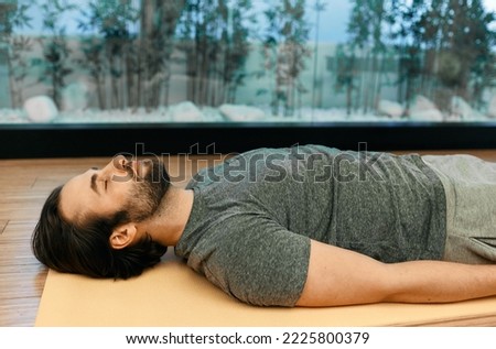 Savasana or corpse dead pose. Handsome man relaxes in motionless corpse pose with closed eyes lying on floor of meditation center Royalty-Free Stock Photo #2225800379