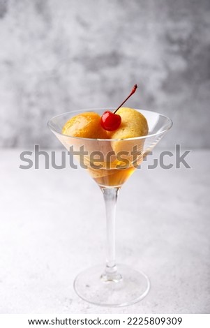 Neapolitan Rum baba (or baba au rum) in a martini glass with a cocktail cherry on a gray background. Small yeast cakes soaked in rum syrup. Traditional Italian pastry. Close-up, selective focus.