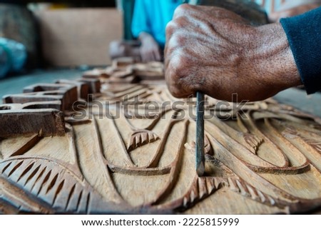 The hand of a woodcarver is carving a wood carving with a chisel Royalty-Free Stock Photo #2225815999