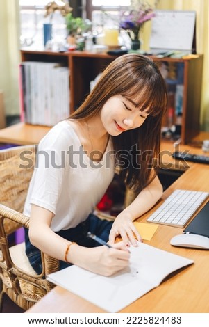 Young adult asian student woman stay at home and study online. Workplace table with laptop computer and book. Domestic lifestyle background with window light on day.