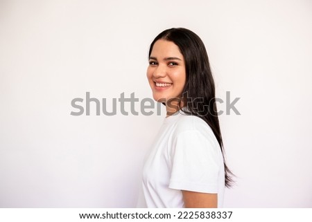 Portrait of candid young woman looking at camera and smiling over white background. Caucasian lady wearing white T-shirt posing in studio. Female beauty concept