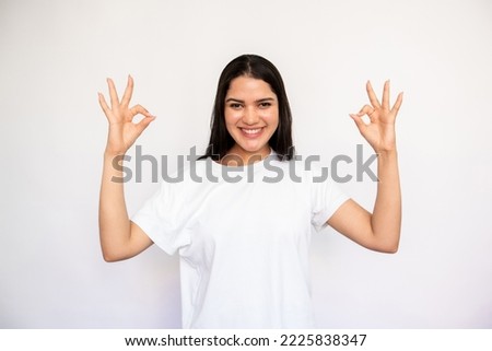 Portrait of happy young woman making ok gesture over white background. Caucasian lady wearing white T-shirt showing agreement sign, looking at camera and smiling. Success and satisfaction concept