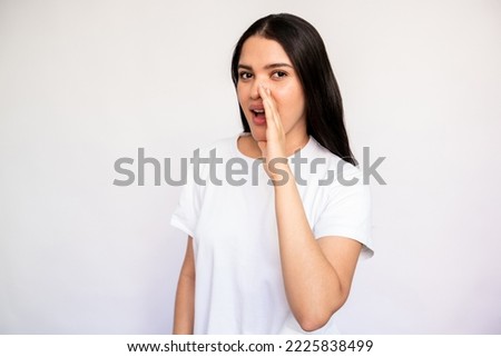 Portrait of young woman whispering secret covering mouth with hand over white background. Caucasian lady wearing white T-shirt telling gossip. Secret and gossip concept