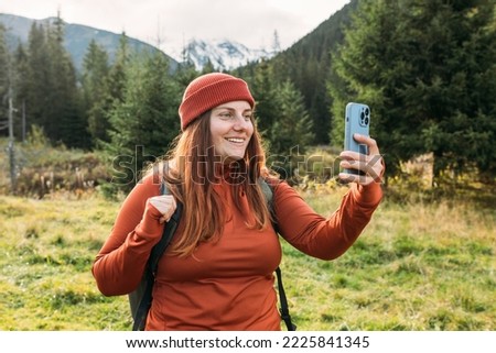 Woman in hat uses a telephone for take pictures, makes selfies and video calls family from home on mountains background. Travel and wanderlust concept. Amazing chill moment