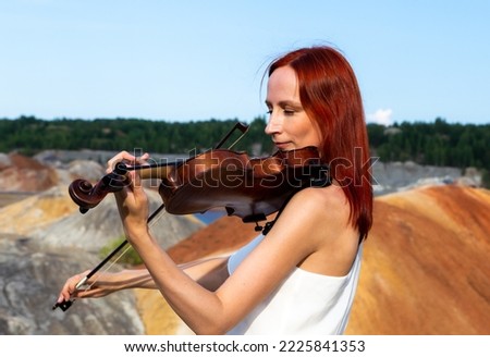 Woman playing violin in red sunset in nature quarry with Martian landscapes