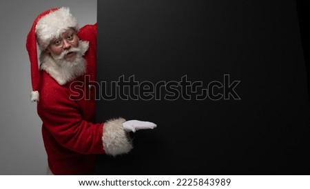 Santa Claus pointing at black paper billboard with copy space for text , surprised facial expression
