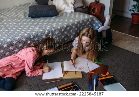 Two girls friends play at home, draw with pencils and felt-tip pens and have fun