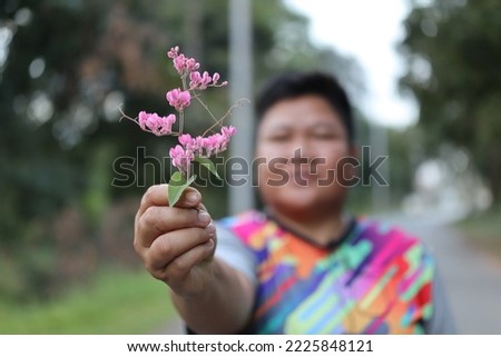 Asian woman holding a pink flower. Raised. Focus on the flower. Blurred background.