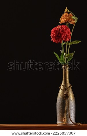 Homemade, silver and gold plated wine bottle vase with a bouquet of zinnia flowers on a dark background