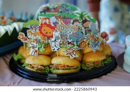 Selected focus photo of a birthday cake which is from a pile of burgers with a zoo theme that has lots of animal pictures