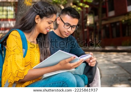 University student friends from different ethnicities holding a book and discussing about studies at a campus.  Royalty-Free Stock Photo #2225861937