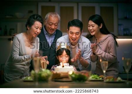 little asian girl making a wish while three generation family celebrating her birthday at home