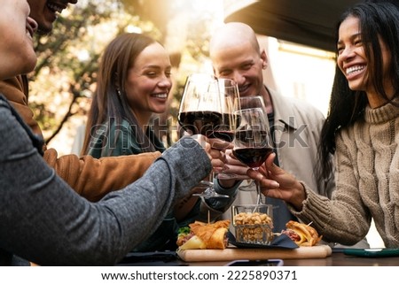 Young smiling friends toasting red wine at restaurant pub at happy hour with appetizers  - Happy people having fun together at winery bar and eating food  - Dinning life style concept. focus on glass 
