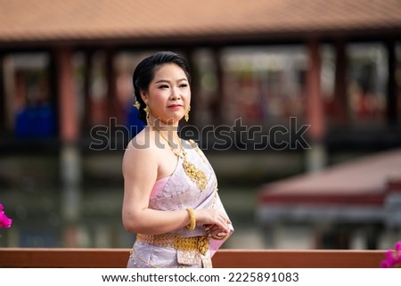 A woman in a traditional Thai costumes is standing on the wooden bridge while being taken a portrait photo shooting.