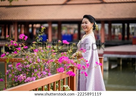 A woman in a traditional Thai costumes is standing on the wooden bridge while being taken a portrait photo shooting.
