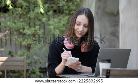A woman are studying online and taking notes on a lecture at an outdoor table