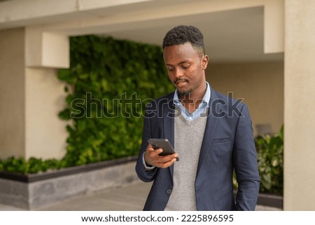 Portrait of handsome black African businessman wearing suit and texting with smart phone
