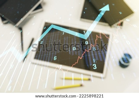 Multi exposure of abstract financial graph with upward arrow and modern digital tablet on desktop on background, top view, financial and trading concept