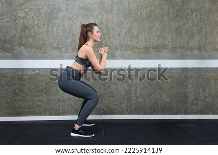 Woman squatting with her arms in front of her chest, trainer shows exercise for glutes at the gym Royalty-Free Stock Photo #2225914139