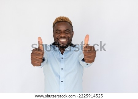 Portrait of cheerful African American man with thumbs up. Happy young male model with blond hair in light blue shirt looking at camera, smiling and showing respect. Advertisement, approval concept