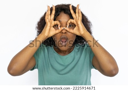 Funny young woman showing finger glasses gesture. Portrait of African American female model in casual T-shirt making glasses with fingers, having fun. Studio shoot, emotion, entertainment concept