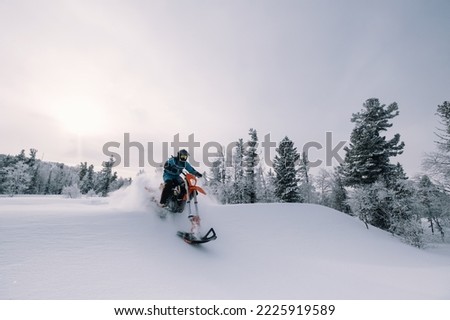 Snowbike rider in mountain valley in beautiful snow powder. Modify dirt bike with snow splashes and trail. Snowmobile sport riding, winter sunny day
