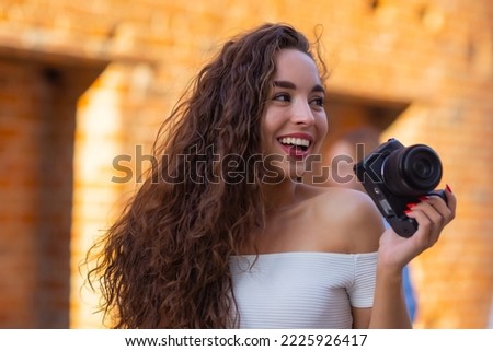 Young attractive female student or tourist using a mirrorless camera while walking in summer city. Woman takes pictures and enjoy weather.