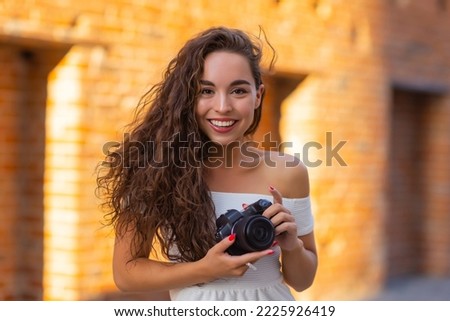 Young attractive female student or tourist using a mirrorless camera while walking in summer city. Woman takes pictures and enjoy weather.