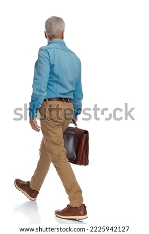 back view of old man in his 60s holding suitcase and walking in front of white background in studio