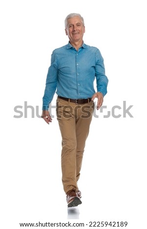 full body picture of happy old man with grizzled hair walking and smiling in front of white background in studio