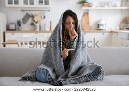 Sick at home. Unhealthy, ill young coughing woman measuring body temperature with electronic thermometer, suffering from pneumonia. Female having cold symptoms fever, chills and difficulty breathing Royalty-Free Stock Photo #2225942325