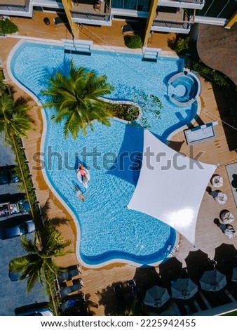 Drone view at the pool with palm trees, a couple of men and women in a swimming pool view from above a tropical garden 