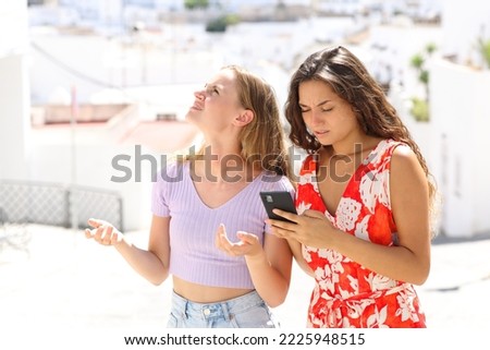 Lost tourists checking smart phone on vacation in a town standing in the street