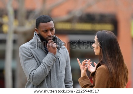 Suspicious man listening a woman talking in winter in the street Royalty-Free Stock Photo #2225948517